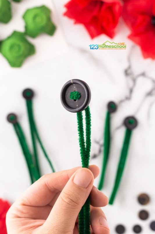 Fold green pipe cleaners in half and carefully thread them through a button. Once you’ve finished, set them aside and repeat the process for more buttons! 