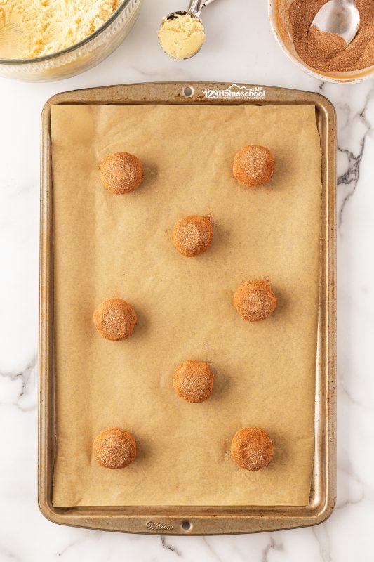Ready to bake those delicious snickerdoodles? Place your cookie dough balls onto a baking sheet lined with parchment paper for easy cleanup.

Tip: For flatter, perfectly baked snickerdoodles, gently press down the center of each dough ball before they head into the oven. This little trick helps them maintain their shape and prevents puffing in the middle. 